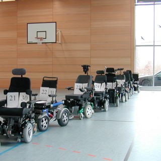 die Turnhalle des Unfallkrankenhauses Berlin mit einer langen Reihe von zu untersuchenden elektrischen Rollstühlen